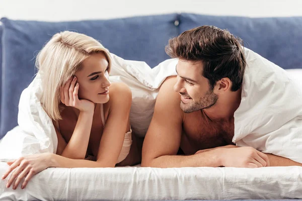 有选择的焦点英俊的男友和有吸引力的女朋友微笑着躺在床上 — 图库照片