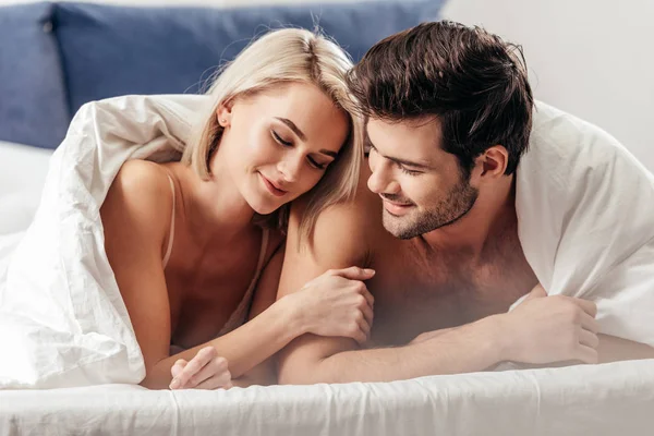 有选择的焦点英俊的男友和有吸引力的女朋友微笑着躺在床上 — 图库照片