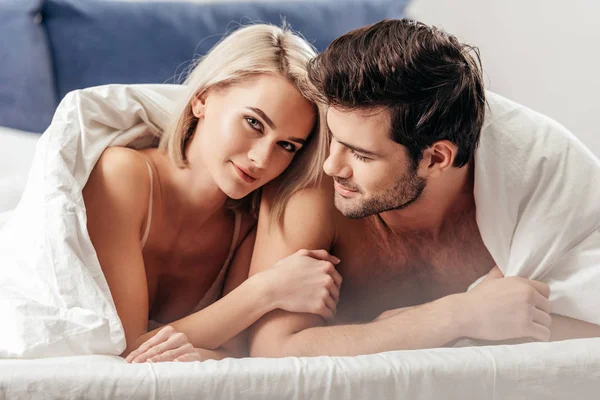 有选择的焦点英俊的男友和有吸引力的女朋友躺在床上 看着相机 — 图库照片