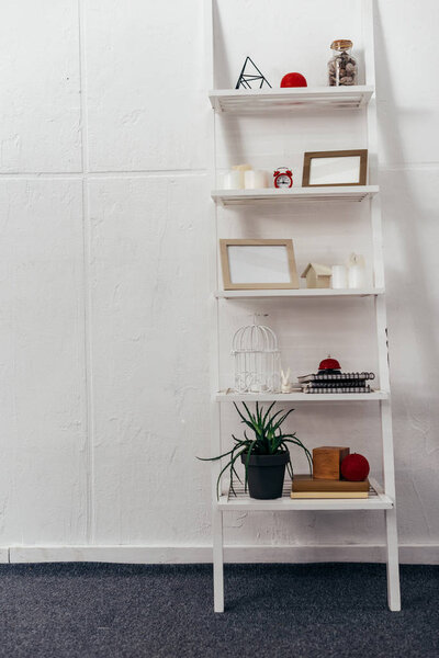 shelves with red clock, wooden frameworks, plant, books, bottle with seashells and candles on white background