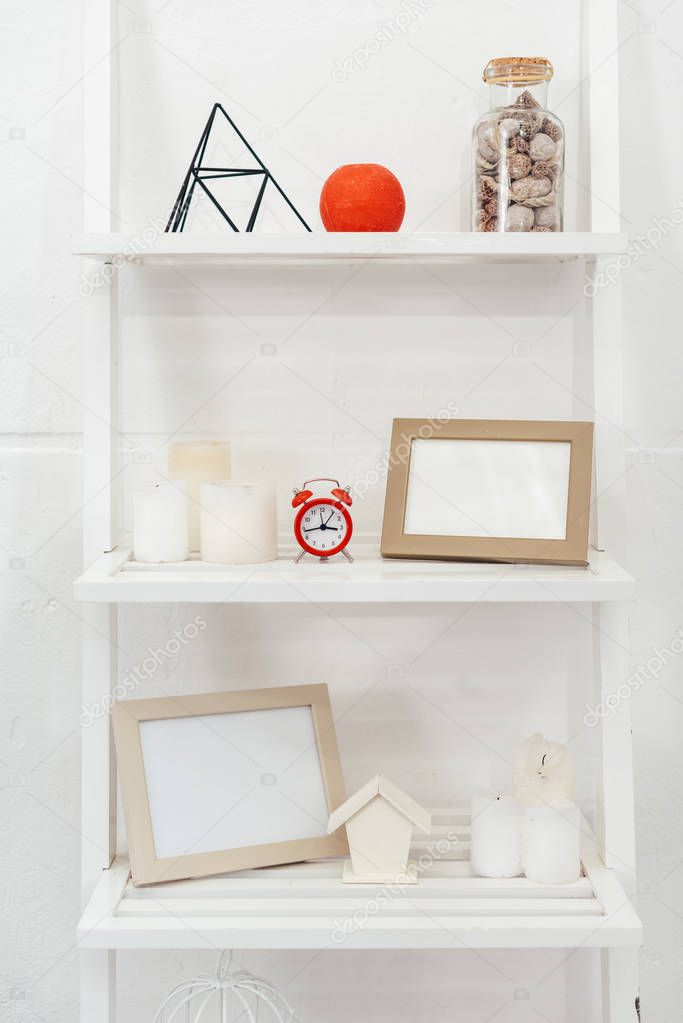 shelves with red clock, wooden frameworks, bottle with seashells and candles on white background