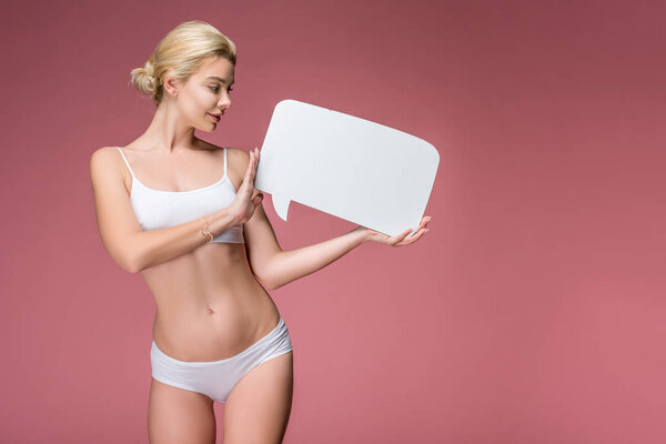 happy young woman in white underwear posing with empty speech bubble, isolated on pink