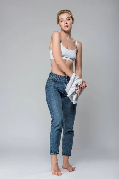 Sottile Ragazza Bionda Jeans Reggiseno Bianco Spogliarsi Isolato Grigio — Foto Stock
