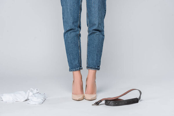 low section view of woman in jeans and high heels undressing isolated on grey 