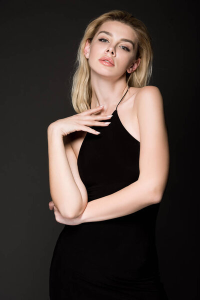 стильная блондинка в черном платье позирует изолированно на черном
