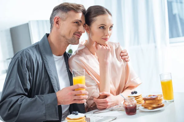 英俊的男人拿着橙汁和拥抱妇女在早餐在早上 — 图库照片
