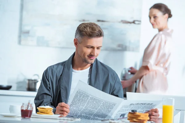 Man Läsa Tidningen Frukost Medan Kvinnan Matlagning Bakgrund — Stockfoto