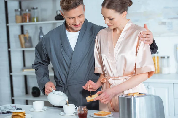 Mand Kåbe Hælde Mens Kvinde Forbereder Toasts Med Marmelade Morgenmaden - Stock-foto
