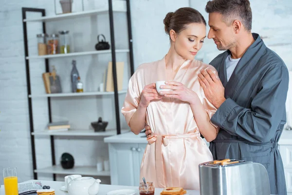 Bell Uomo Accappatoio Che Abbraccia Bella Donna Con Tazza Cucina — Foto Stock