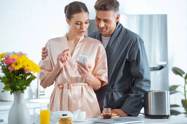 Hermosa Pareja Adulta Túnicas Usando Teléfono Inteligente Durante Desayuno Cocina — Foto de Stock