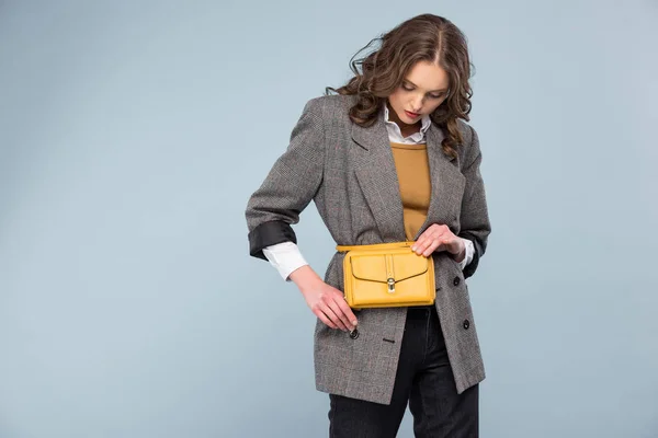 beautiful stylish woman in formal wear holding bag and posing isolated on grey with copy space