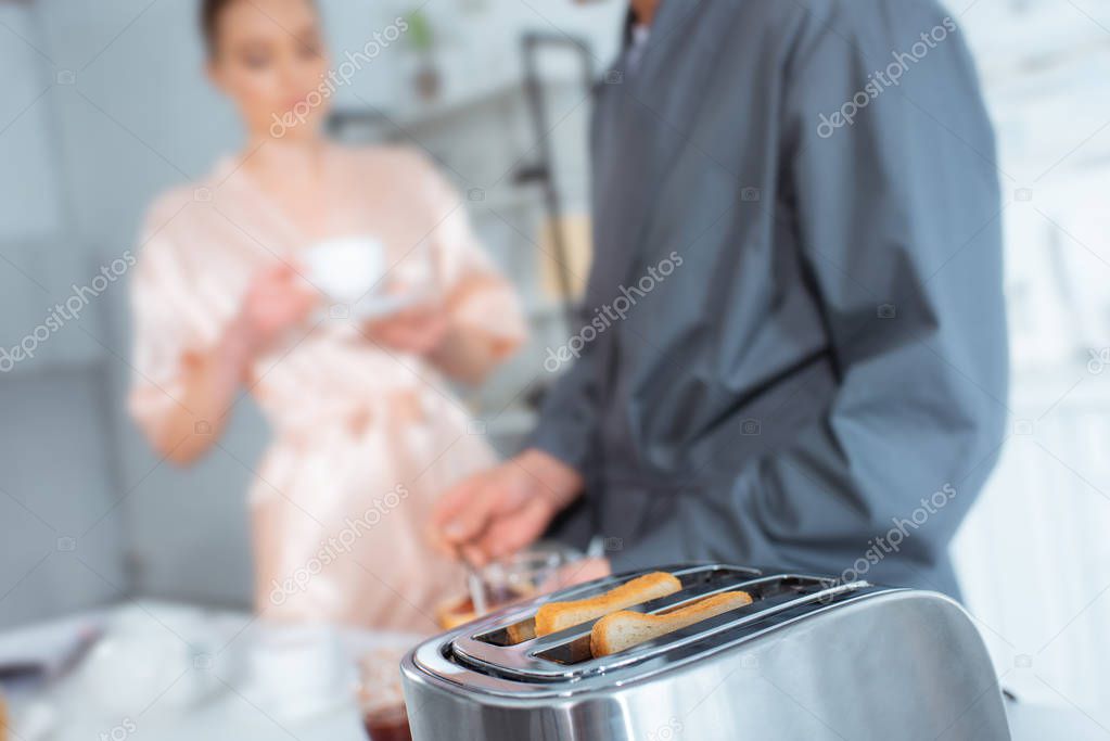 selective focus of toaster with toasts and couple during breakfast on background