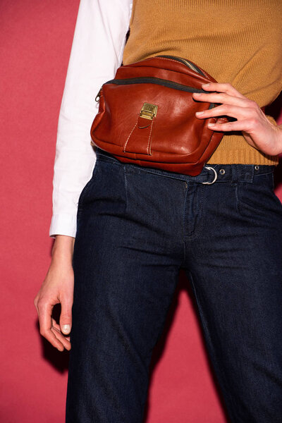 partial view of woman holding leather bag on red background