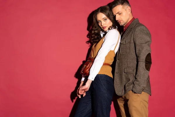 beautiful fashionable couple in formal wear posing on red background with copy space