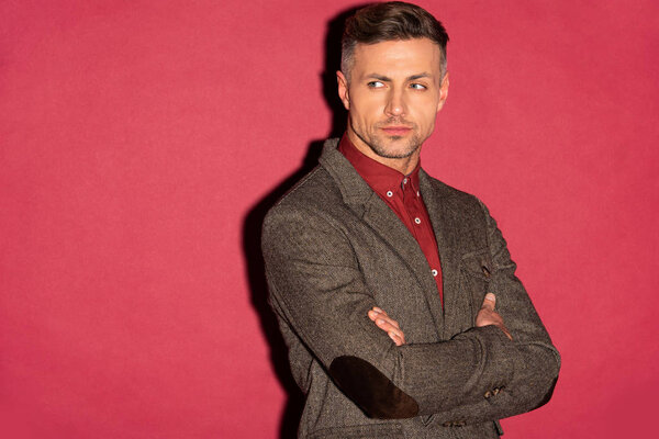 handsome stylish man in formal wear with arms crossed looking away on red background