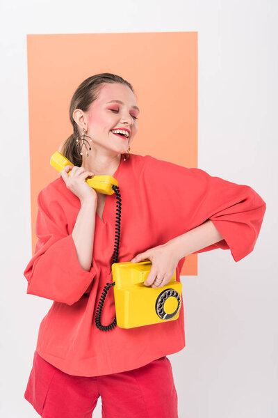 happy stylish girl holding retro telephone and posing with living coral on background