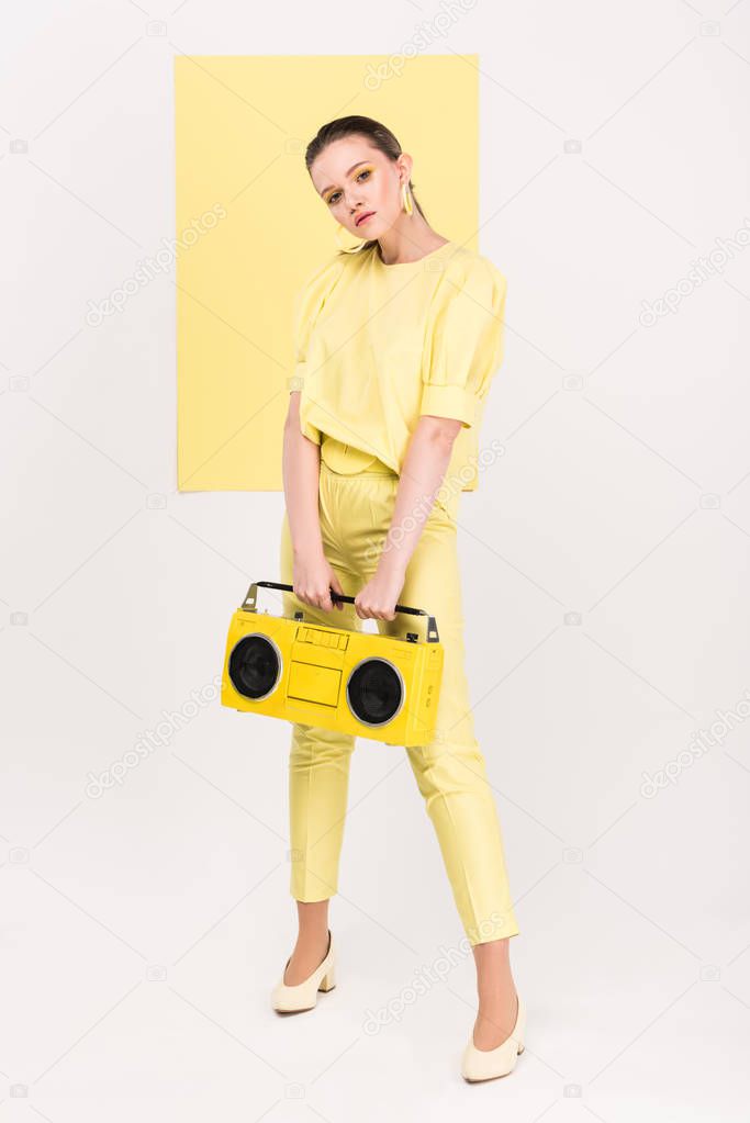 stylish girl holding retro boombox and posing with limelight on background