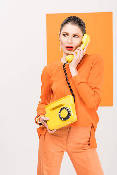 surprised fashionable young woman talking on retro telephone and posing with turmeric on background