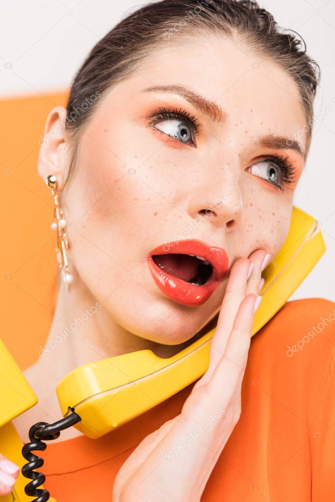 beautiful surprised woman talking on retro telephone and touching face with turmeric on background