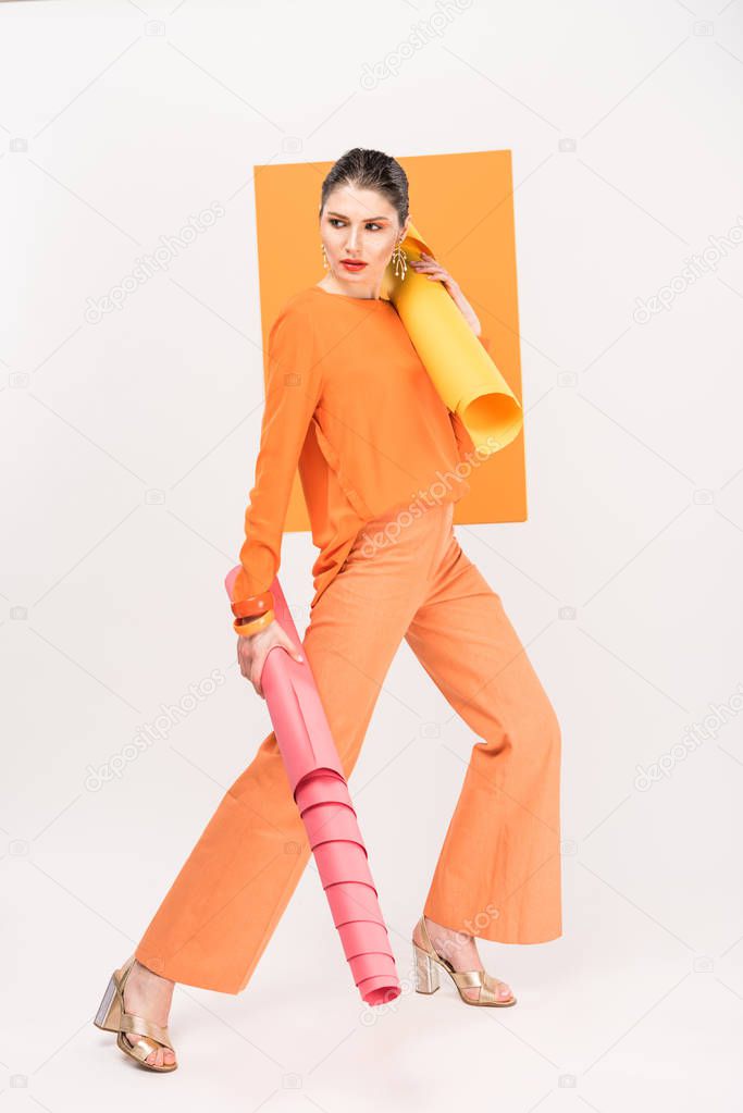 stylish young woman holding paper rolls, looking away and posing with turmeric on background