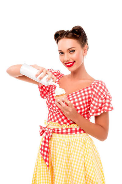 Beautiful pin up girl applying whipped cream on cupcake isolated on white