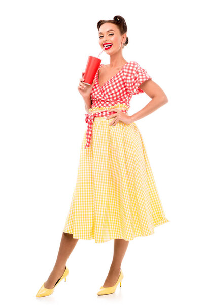 Beautiful pin up girl drinking from paper cup with straw while standing on high heels isolated on white