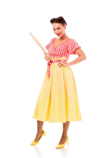 Smiling stylish pin up girl holding rolling pin and looking at camera isolated on white