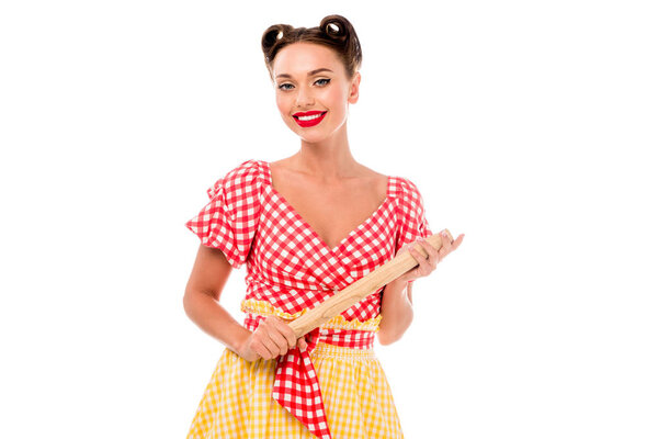 Smiling stylish pin up girl holding rolling pin and looking at camera isolated on white