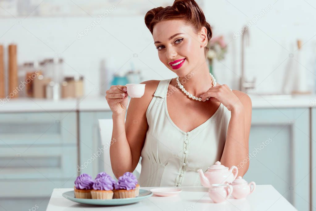 Smiling pin up girl in pearl necklace drinking coffee 