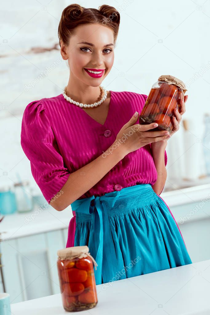 Smiling pin up girl standing at kitchen table and holding canned tomatoes 