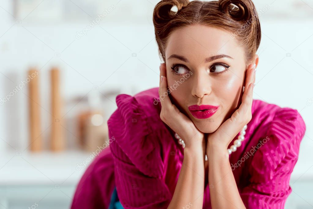 Beautiful pin up girl leaning up on kitchen table and holding head in hands