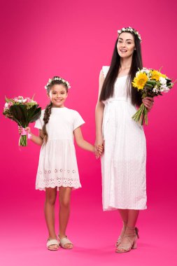 tam uzunlukta görünümünü güzel mutlu anne ve kızı beyaz elbiseler ve buketleri tutarak ve pembe kameraya gülümseyen çiçek çelenk