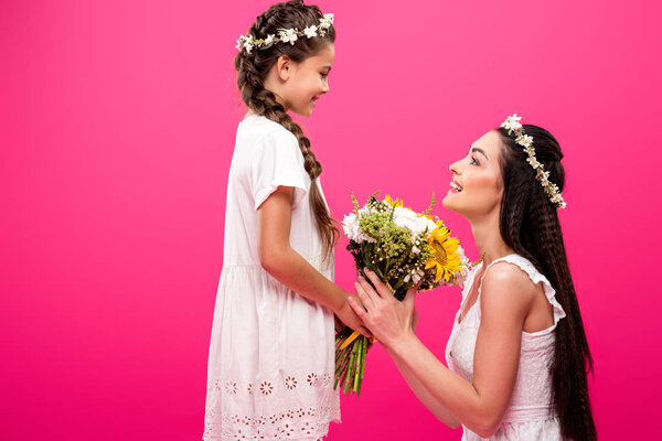 side view of beautiful happy mother and daughter holding bouquet of flowers and smiling each other isolated on pink