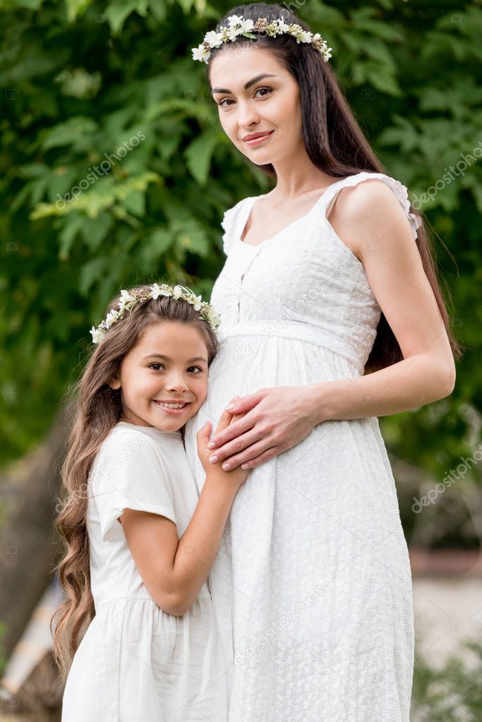 adorable happy child hugging pregnant mother and smiling at camera in park 