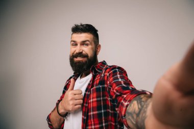 alma selfie, gri izole süre kadar kareli gömlek gösteren başparmak sakallı adam gülümseyen