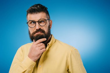 suspicious bearded man in eyeglasses isolated on blue