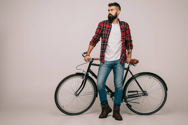 bearded man in checkered shirt standing at bike on grey