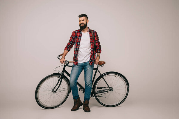 happy man in checkered shirt posing with bicycle on grey