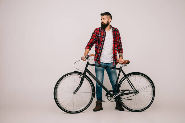 bearded man in checkered shirt posing with bicycle on grey