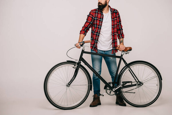 cropped view of man in checkered shirt posing with bicycle on grey