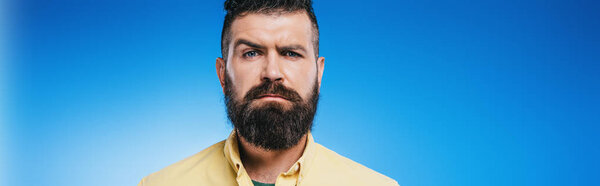 suspicious bearded man looking at camera isolated on blue