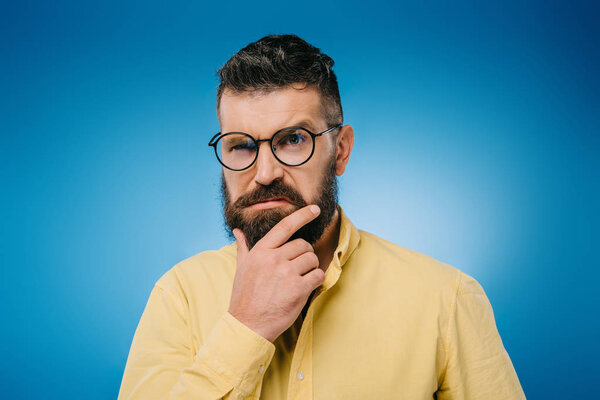 suspicious bearded man in glasses isolated on blue