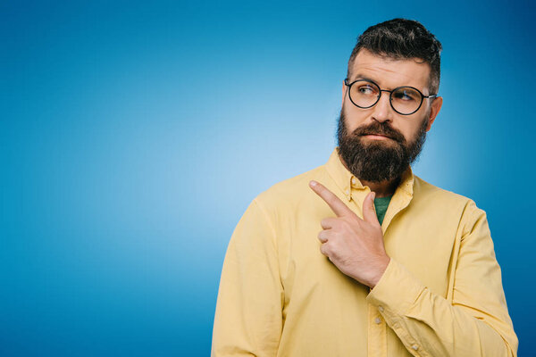 handsome bearded man in eyeglasses pointing isolated on blue