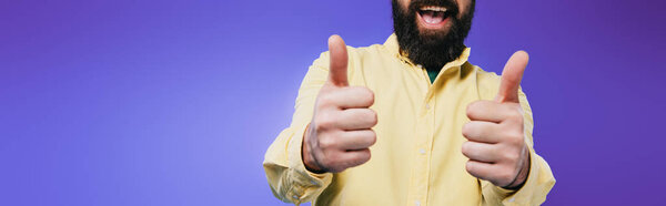 cropped view of smiling man showing thumbs up isolated on purple