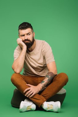 yeşil üzerinde oturan sıkılmış yakışıklı sakallı adam