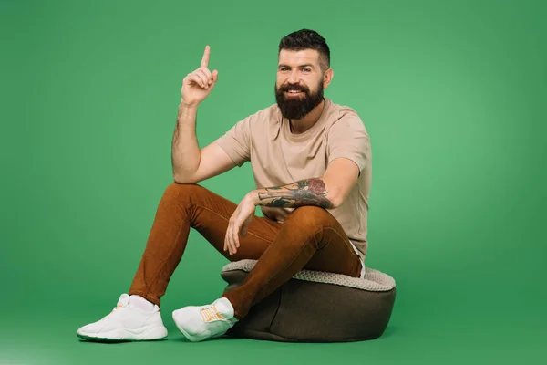 Sorrindo Bonito Barbudo Homem Apontando Para Cima Sentado Verde — Fotografia de Stock