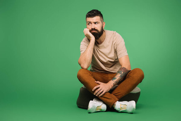 bored tattooed bearded man sitting on green