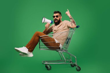 alışveriş sepeti yeşil izole otururken yukarıyı megafon ile sakallı adam