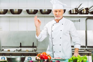 tek tip kameraya görünümlü ve ok işareti Restoran mutfağında gösterilen yakışıklı gülümseyen erkek Şef