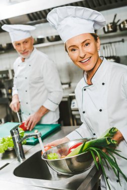 güzel kadın ve erkek şefler içinde Restoran mutfağında yemek sırasında kruvaze ceketler 